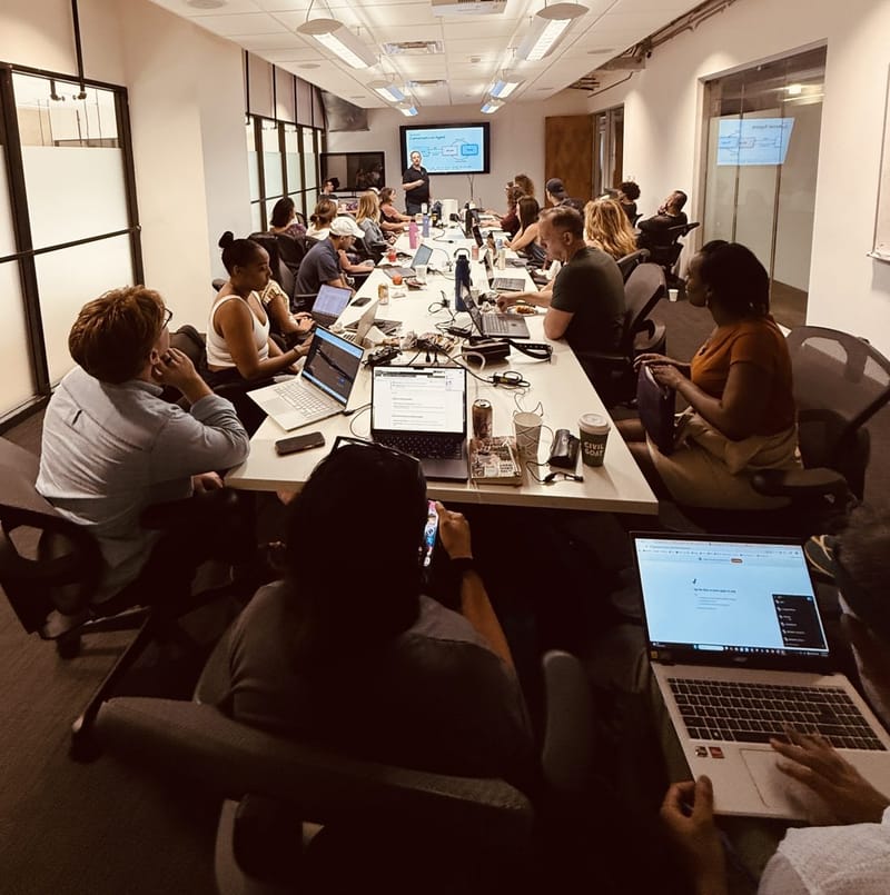 Members of the AI Implementation Club building on their laptops during a session while an instructor presents at the screen